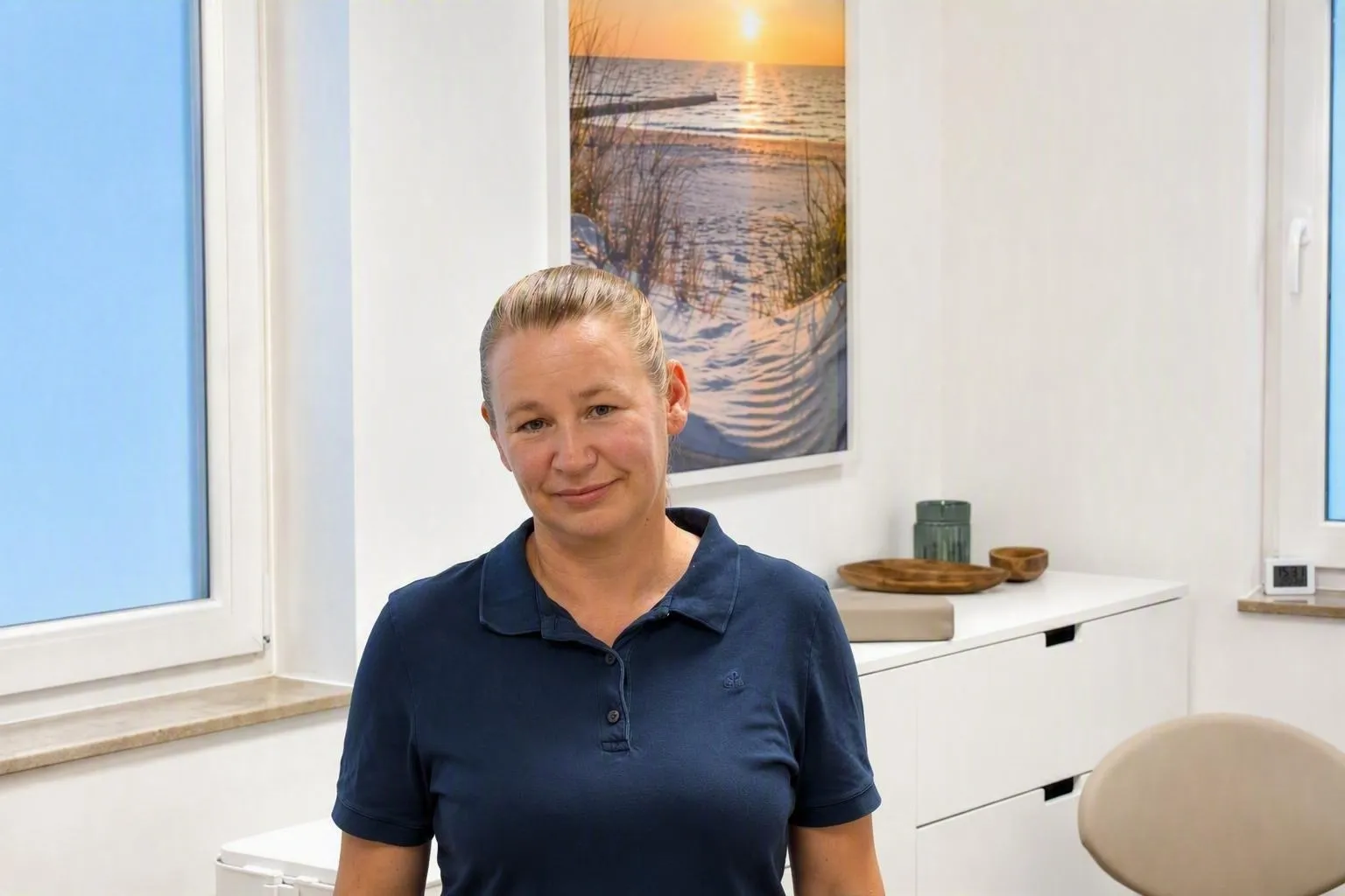 Jeannette Stegmann in ihrem hellen Behandlungsraum, im Hintergrund ein Bild von Strand und Meer